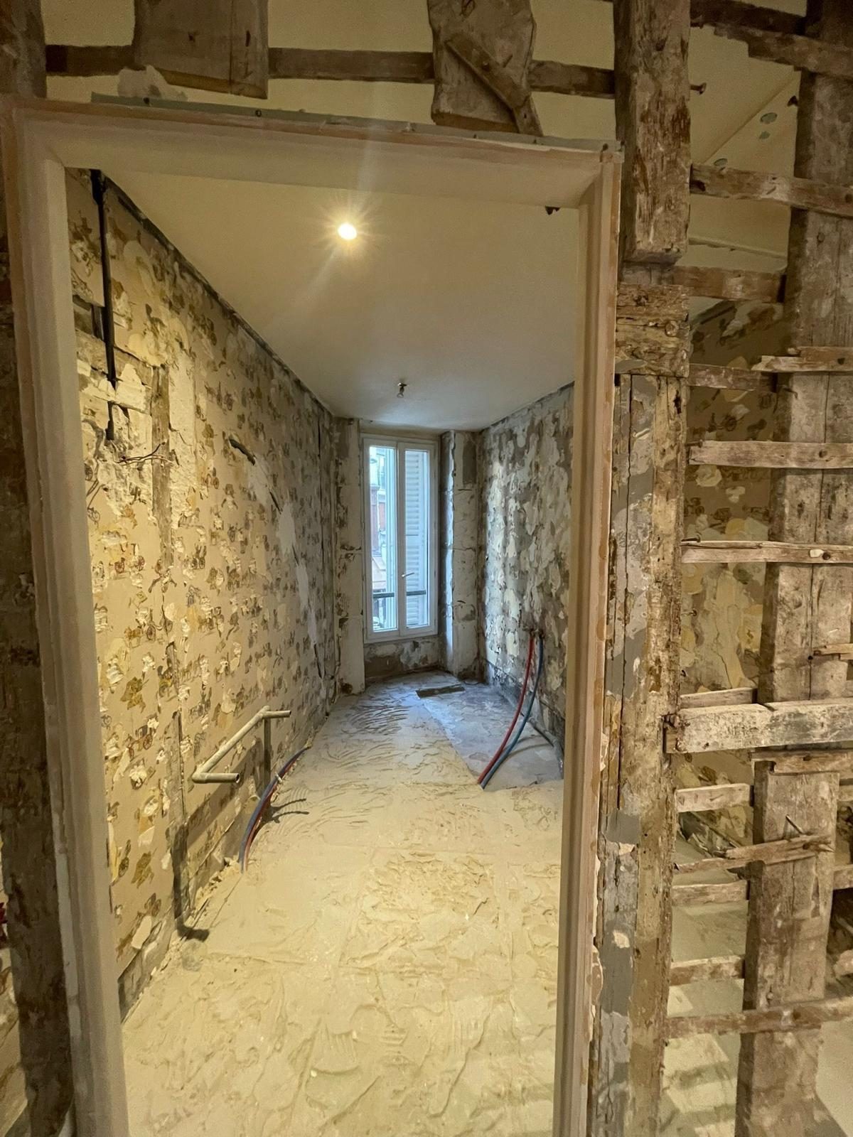 Pièce d'un logement ancien mise à nu : murs décapés, cloison en pan de bois apparente, alimentations neuves en pied de mur