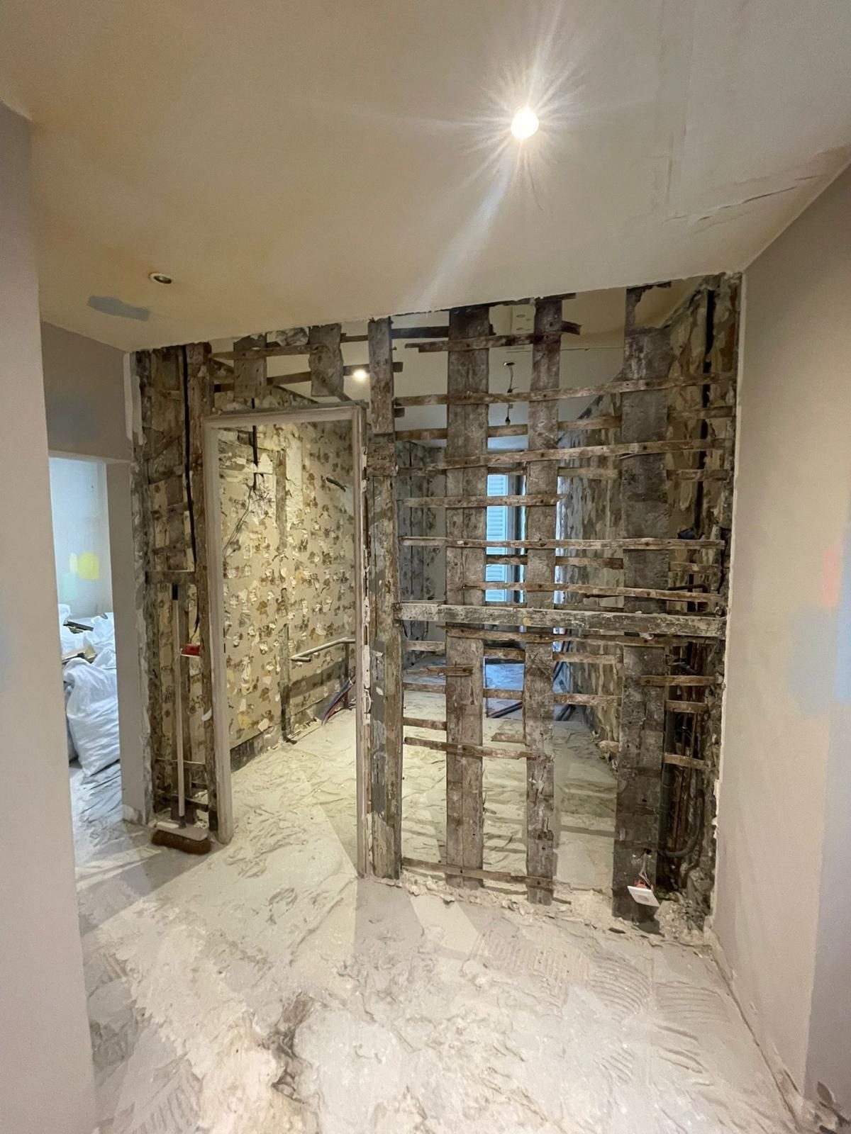 Démolition d'une cloison dans le couloir d'un appartement occupé, pièce voisine protégée sous bâches : la phase la plus bruyante pour l'immeuble. Chantier réel des équipes partenaires.