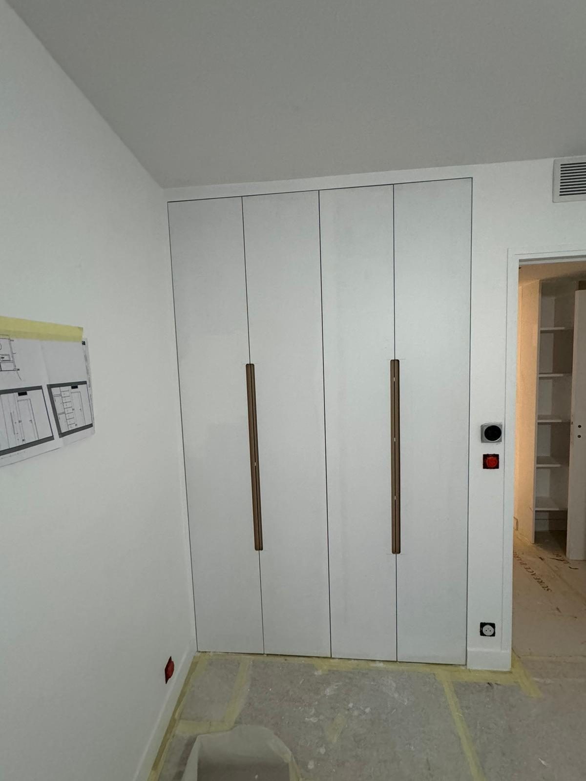 Plans d'exécution affichés sur le chantier, à côté d'un dressing laqué blanc en cours de finition