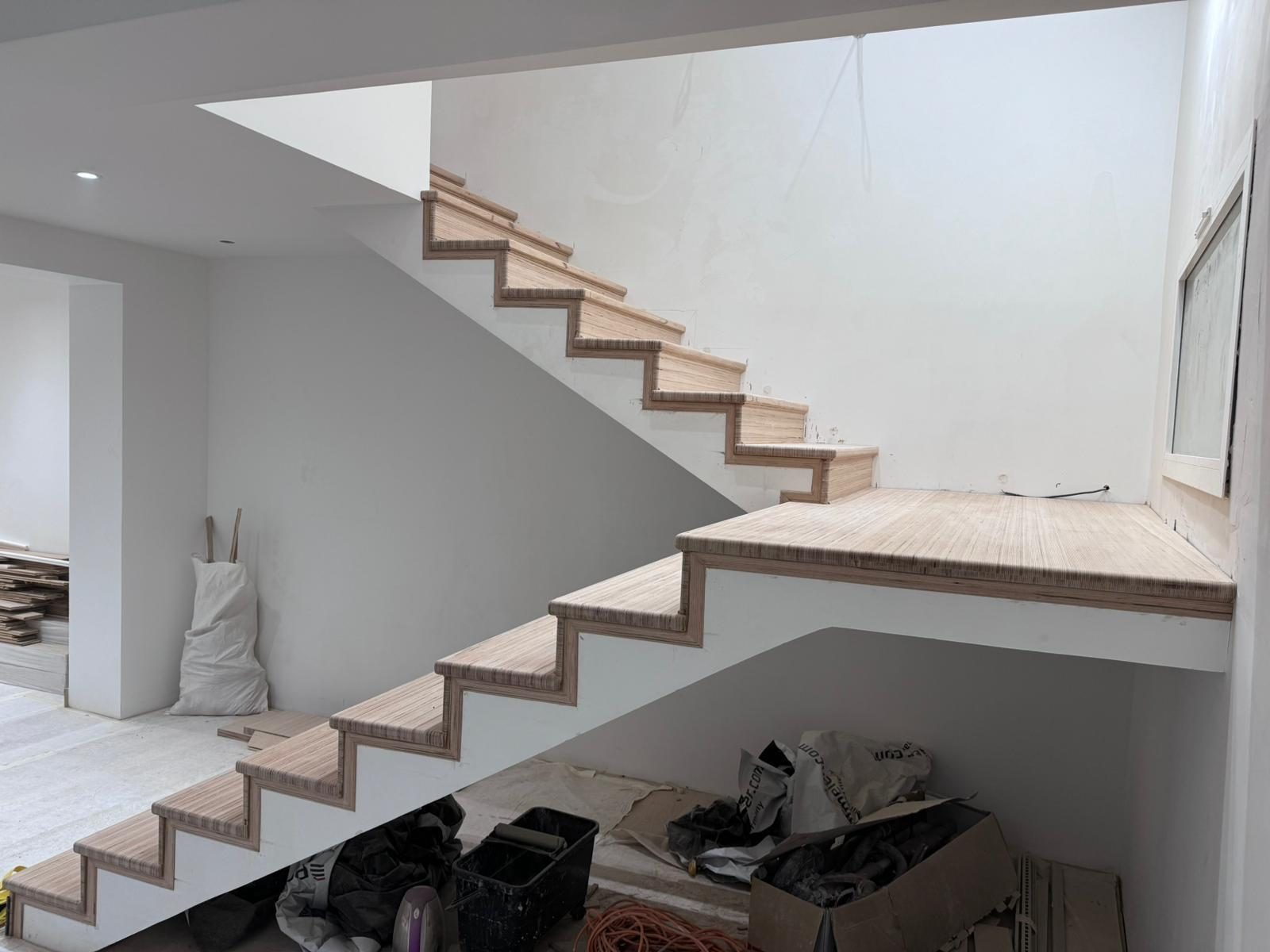 Escalier vu de profil, volée et palier intermédiaire en contreplaqué brut portés par un limon plein enduit en blanc
