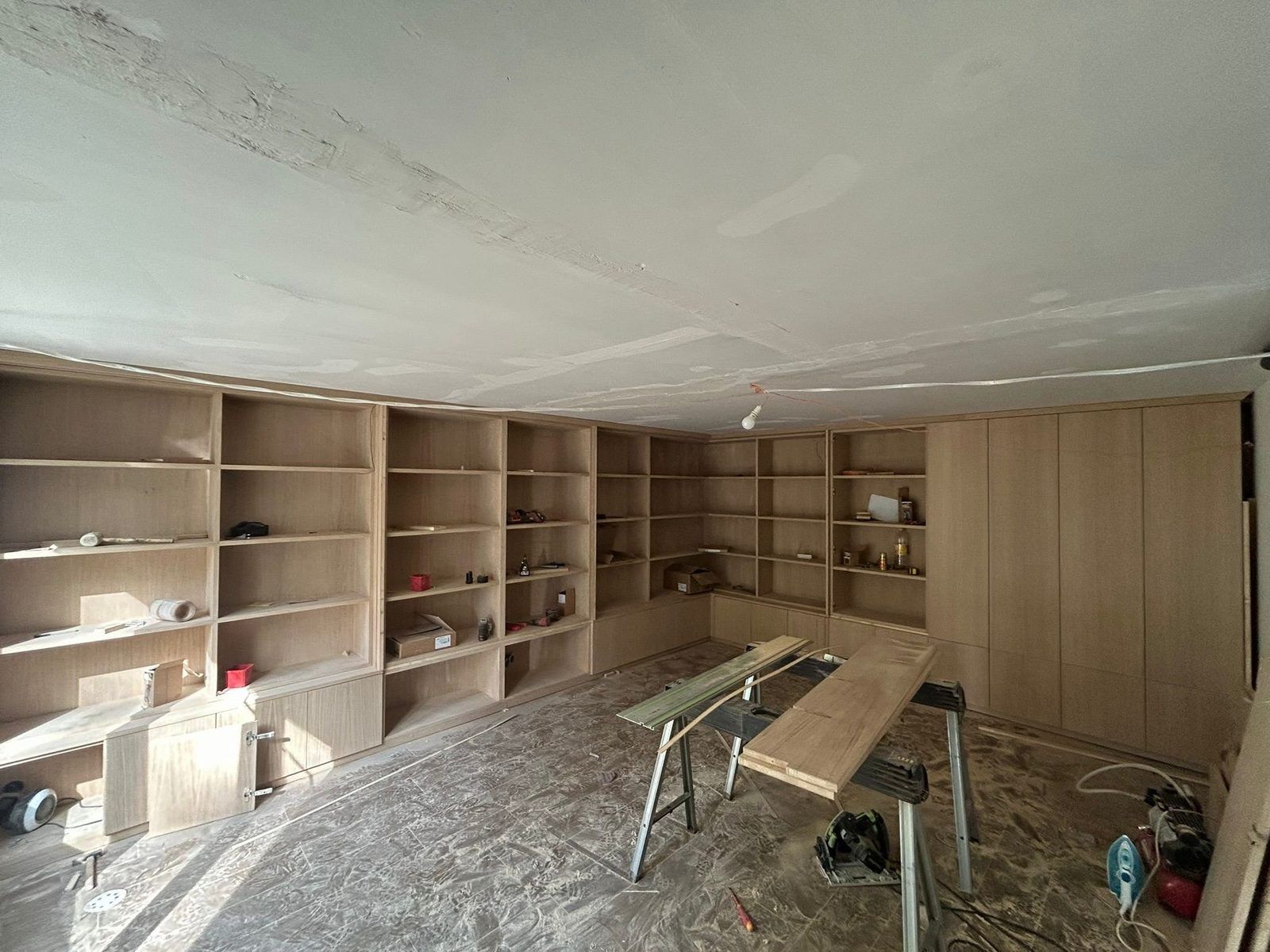 Une pièce entière transformée en atelier le temps de la pose : tréteaux, scie posée au sol, ampoule provisoire au plafond et sol entièrement recouvert. C'est cette emprise-là qu'il faut annoncer avant le premier jour. Chantier réel des équipes partenaires.