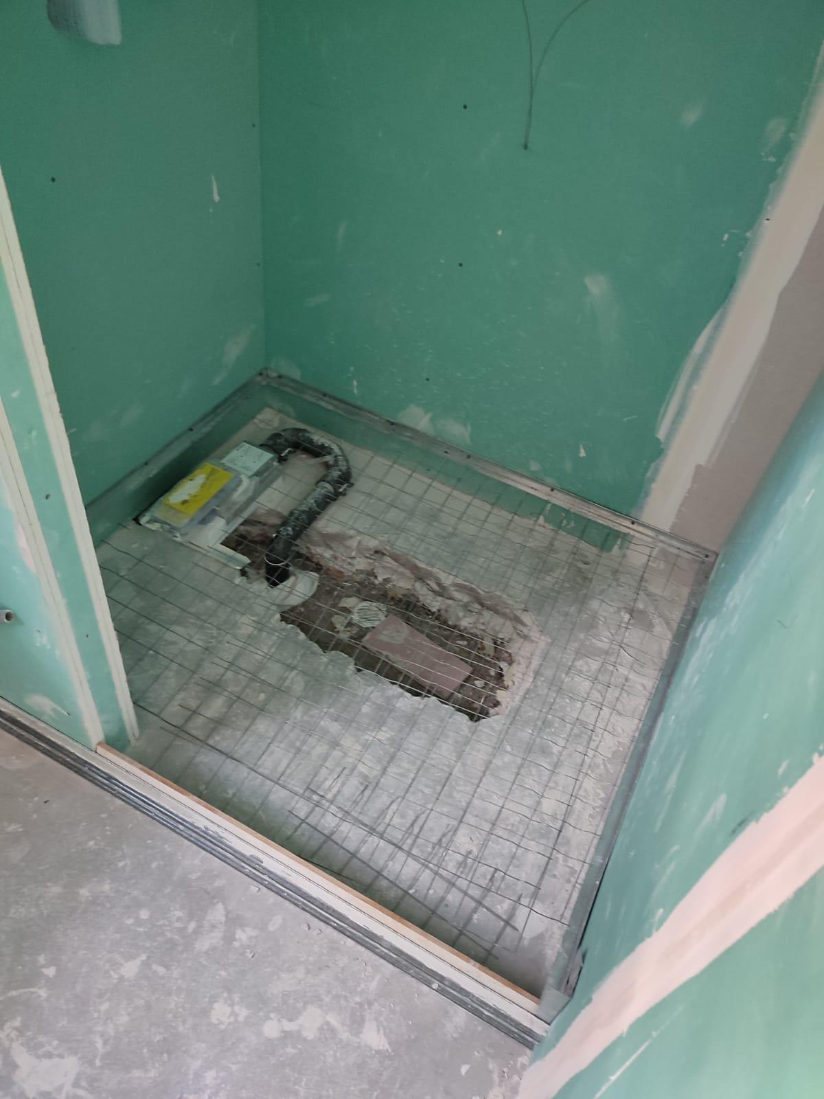 Sol de douche à l'italienne en préparation : treillis d'armature sur la dalle, évacuation en attente, cloisons en plaques hydrofuges