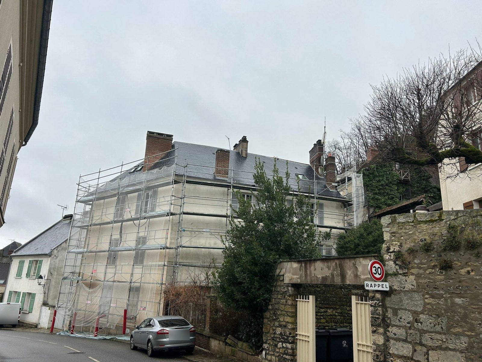 Immeuble ancien à toiture d'ardoise entièrement échafaudé pour un ravalement de façade, dans une rue de centre-bourg