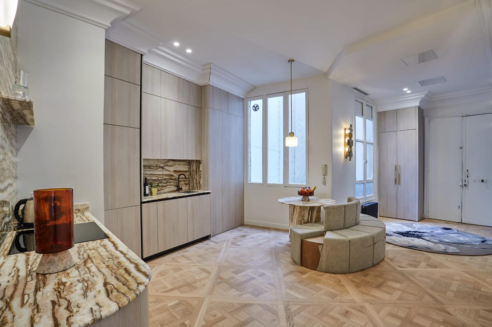 Cuisine ouverte sur le séjour : colonnes en bois clair sans poignée, plan de travail et crédence en onyx, retour de plan arrondi, parquet en panneaux de Versailles. Chantier réel des équipes partenaires.