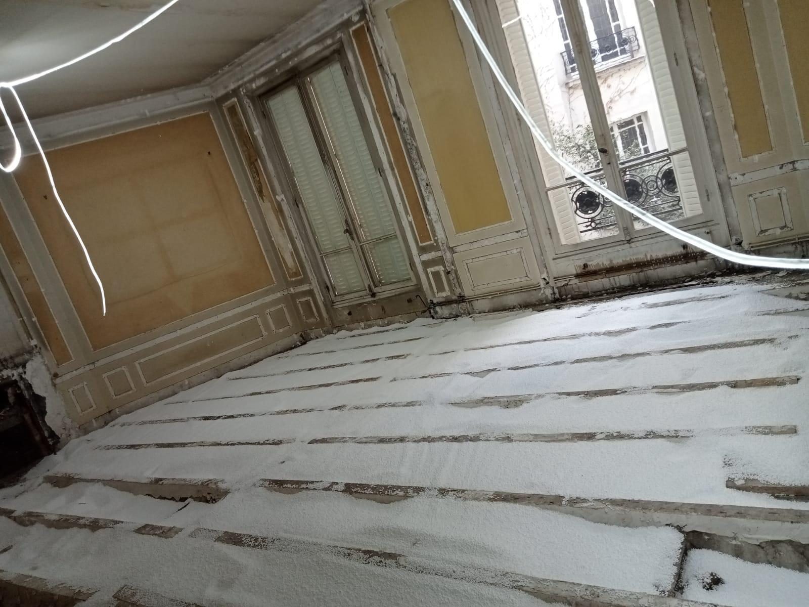 Granulés isolants versés entre les lambourdes d'un plancher ancien, boiseries d'origine et fenêtres encore en place