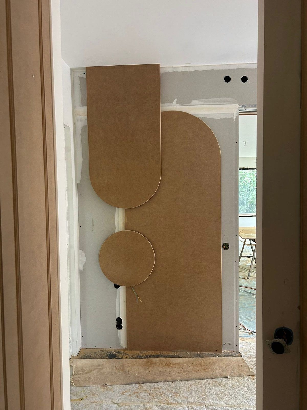 Pièces découpées sur mesure — un arrondi et un disque en panneau — présentées contre la cloison avant fixation, boîtiers électriques encore apparents : format et calepinage se valident avec le poseur avant la commande. Chantier réel des équipes partenaires.