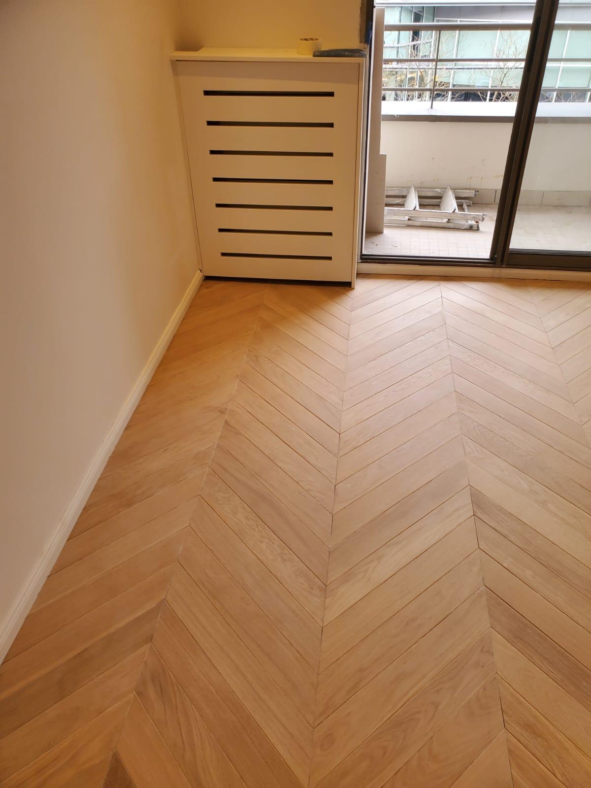 Parquet chêne à chevrons posé et cache-radiateur à lames en place : un sol de ce type se commande longtemps avant sa date de pose, et se pose parmi les tout derniers lots. Chantier réel des équipes partenaires.
