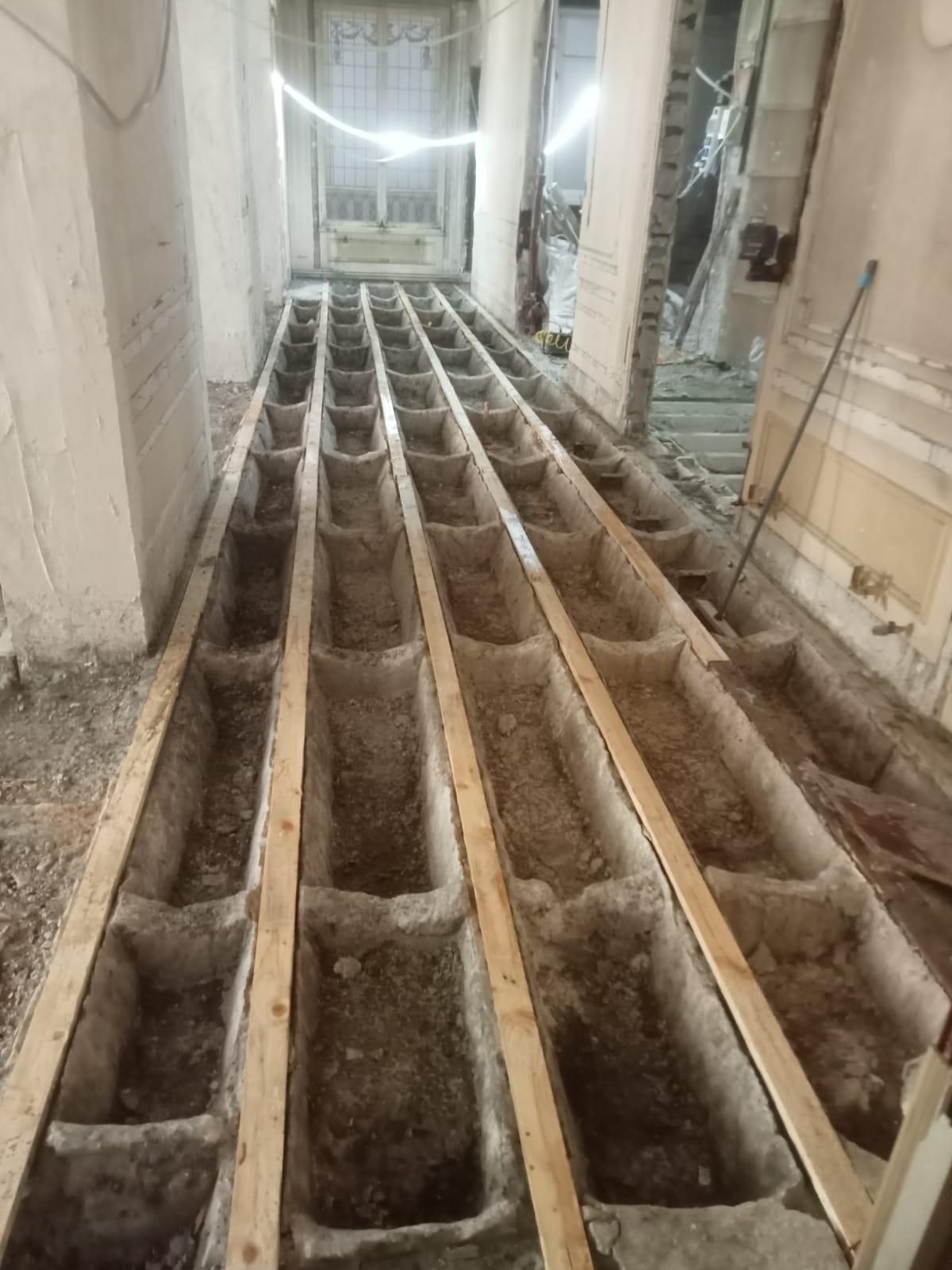 Plancher mis à nu : solives, remplissage entre solives et planches de circulation posées pour travailler dessus. Un niveau supplémentaire charge d'abord ces planchers, avant les murs, puis les fondations. Chantier réel des équipes partenaires.