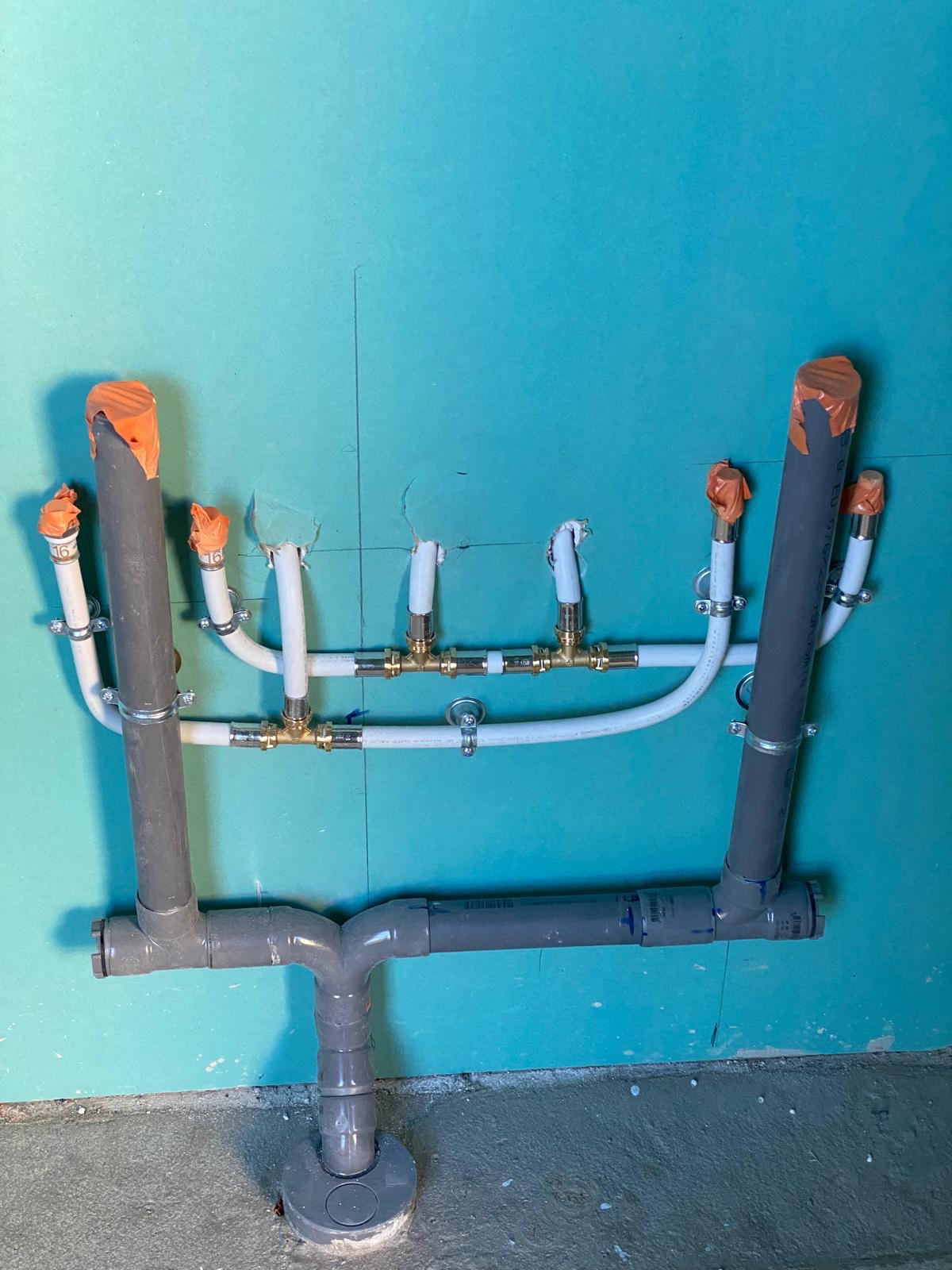 Attentes d'alimentation en multicouche et évacuations PVC laissées bouchées sur un doublage hydrofuge, chantier réel