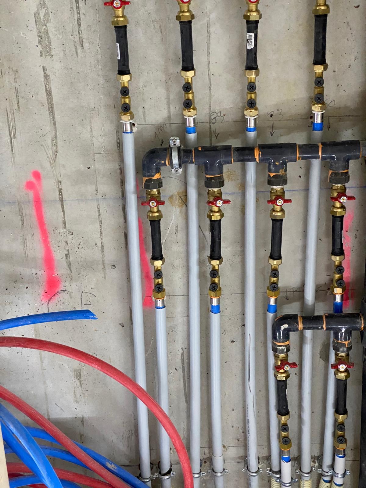 Distribution de plomberie apparente sur voile béton brut avec vannes quart de tour rouges et raccords à sertir, chantier réel