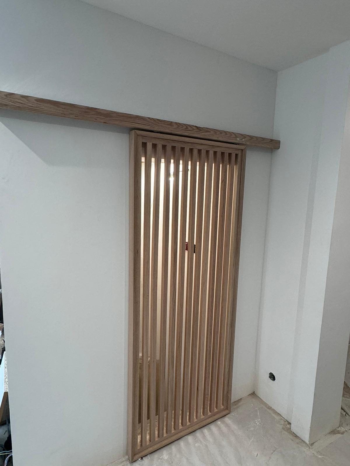 Détail réel d'une porte coulissante à claustra en chêne massif, posée dans un appartement en rénovation