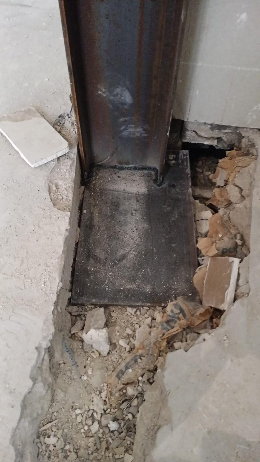 Pied de poteau acier soudé sur sa platine, posé au fond d'un plancher ouvert lors d'une ouverture de mur porteur, gravats autour