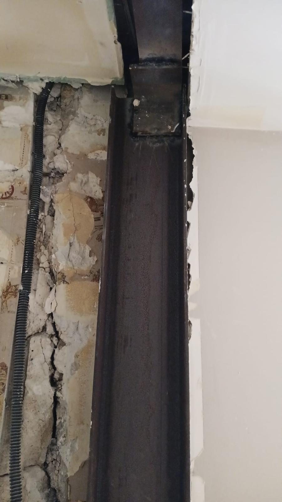 Ouverture de mur porteur en cours : poteau acier soudé sous une poutre de reprise, mur dégarni jusqu'à la pierre et gaine électrique apparente