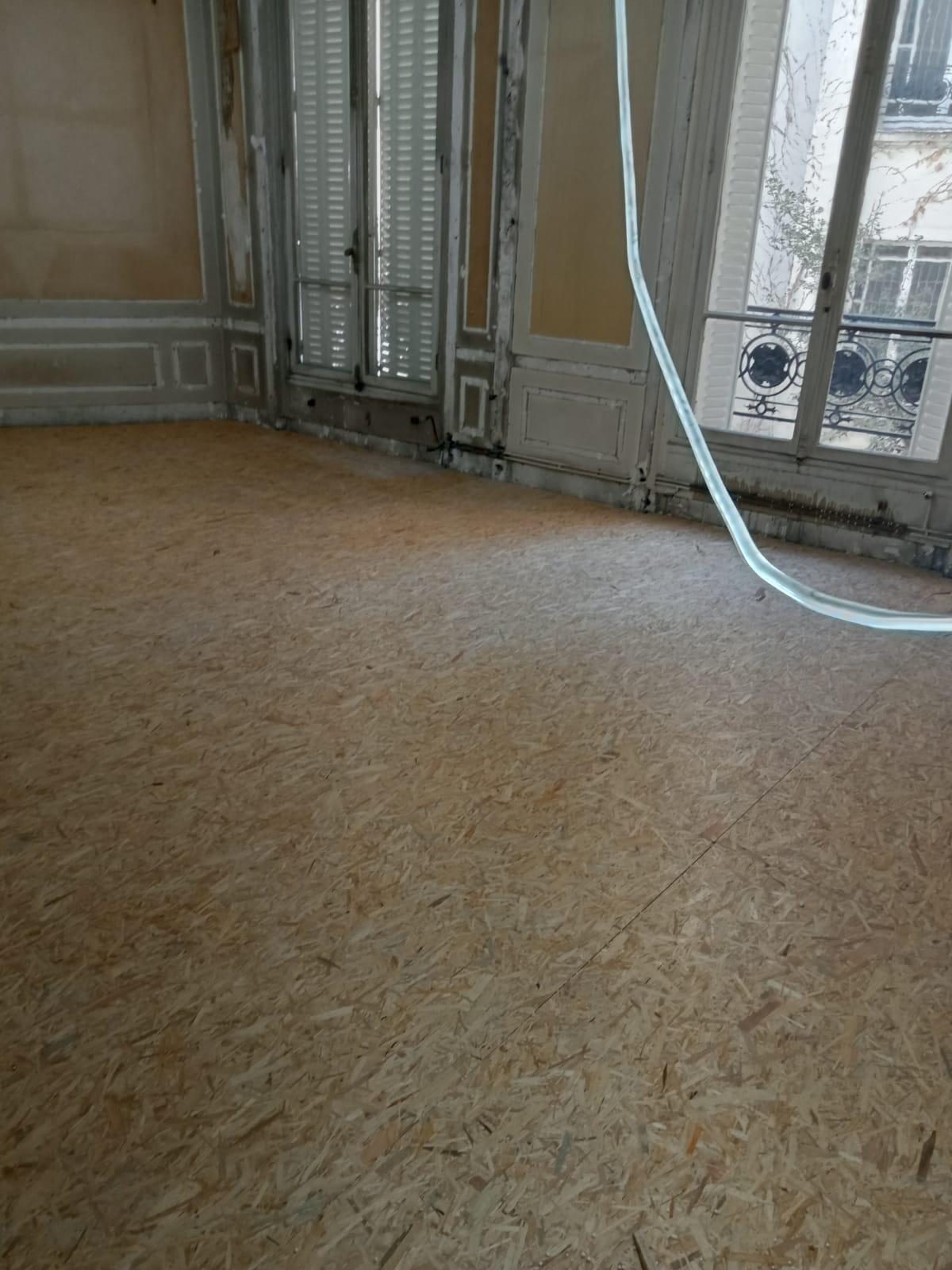 Panneaux OSB posés sur tout le plancher d'un salon haussmannien, boiseries et volets intérieurs en place