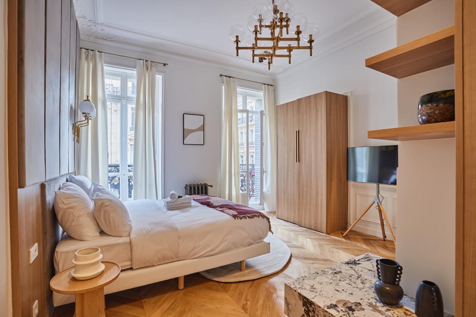 Chambre d'un appartement haussmannien rénové : moulures et corniche conservées, parquet chêne posé à chevrons, grandes fenêtres, armoire en chêne sur mesure