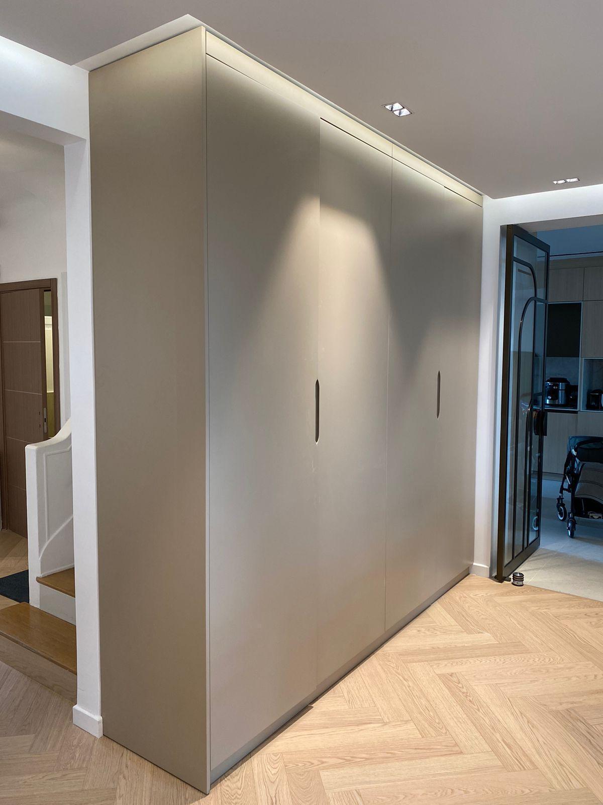 Rangement intégré sur mesure dans une entrée : armoires toute hauteur gris taupe sans poignée, éclairage encastré, parquet à chevrons