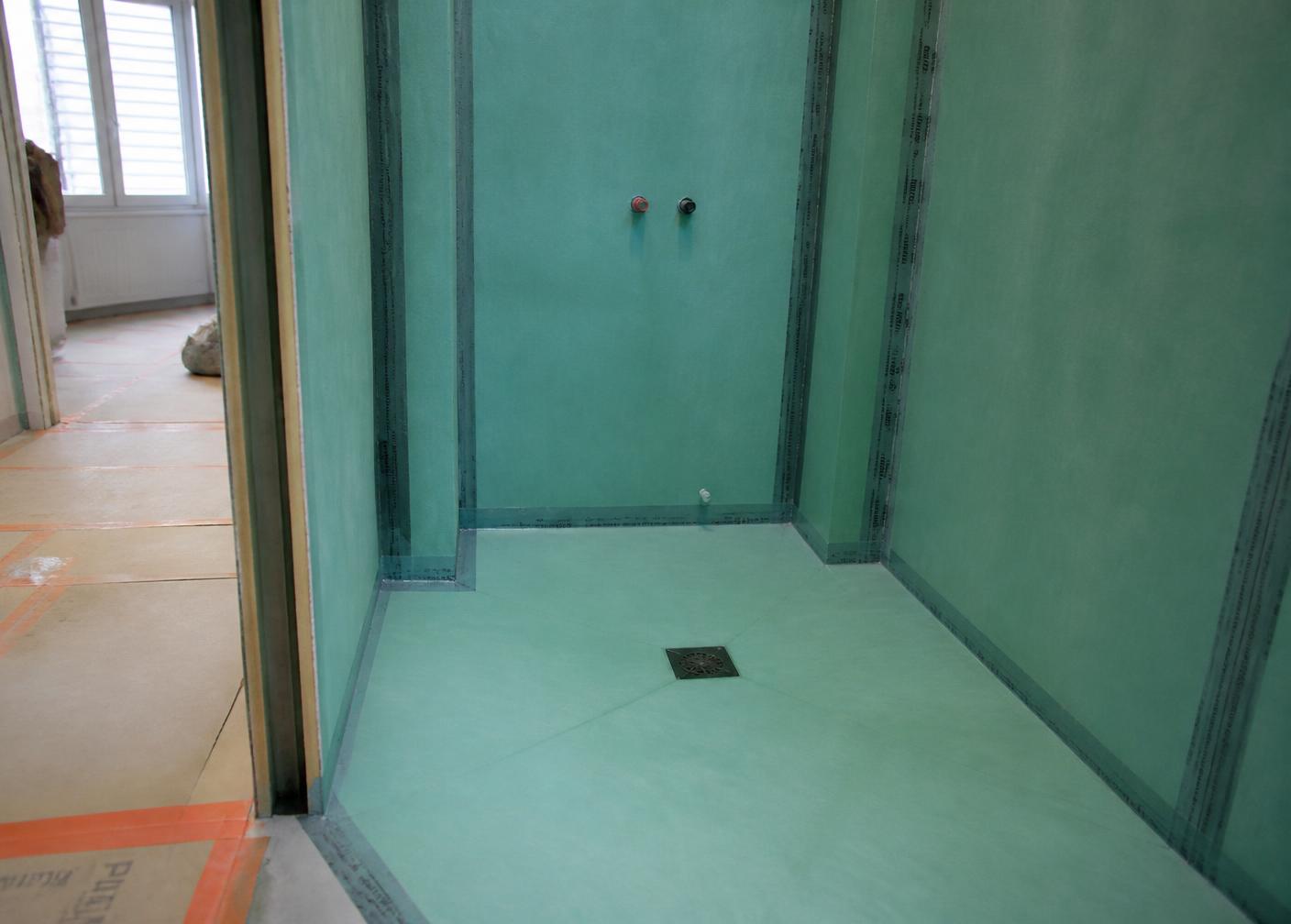 Salle d'eau avant carrelage : étanchéité liquide verte appliquée en plein sur les murs et le sol, bandes de renfort dans tous les angles, siphon de sol au centre