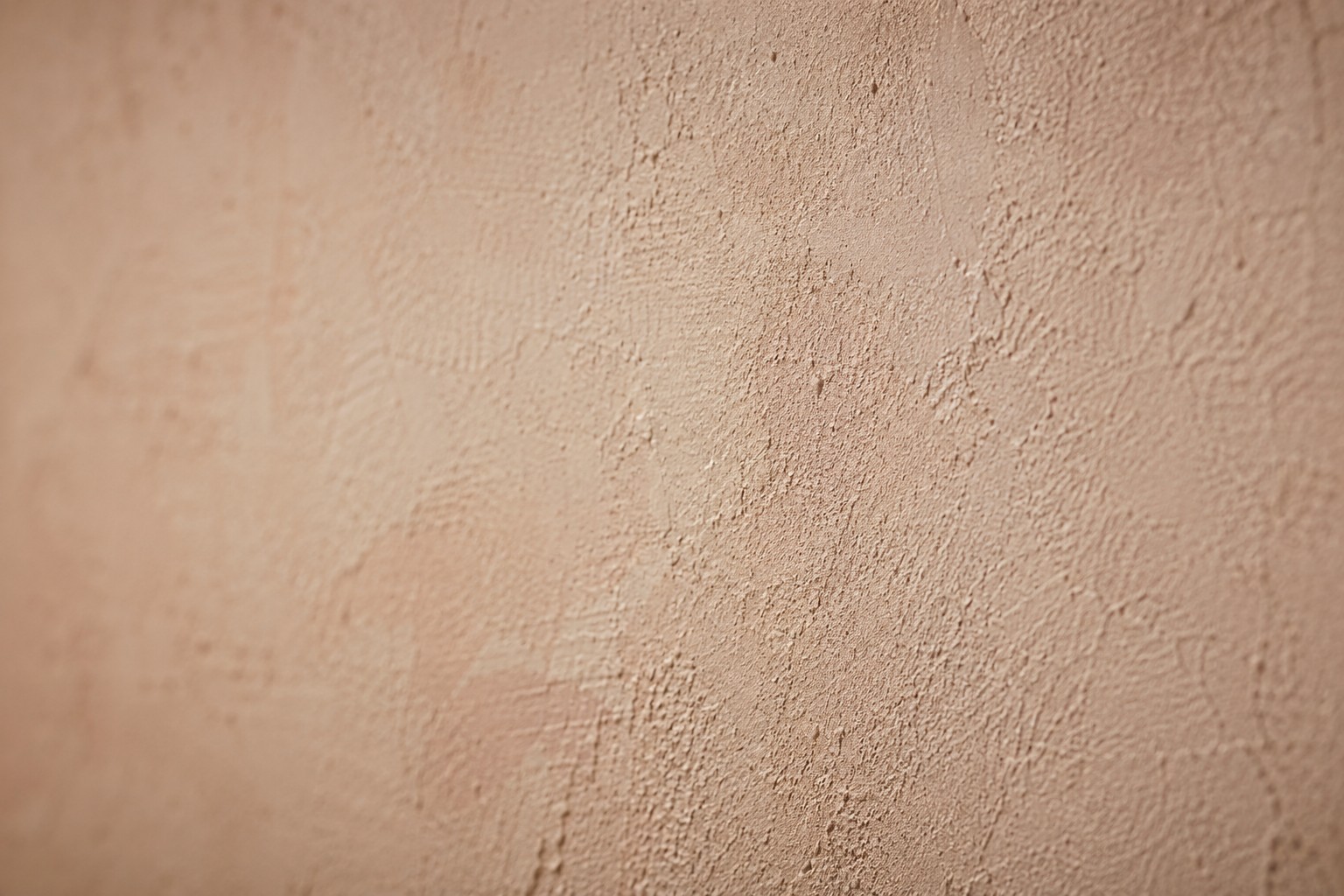 Gros plan sur la texture d'un enduit à la chaux beige rosé, relief mat de la taloche