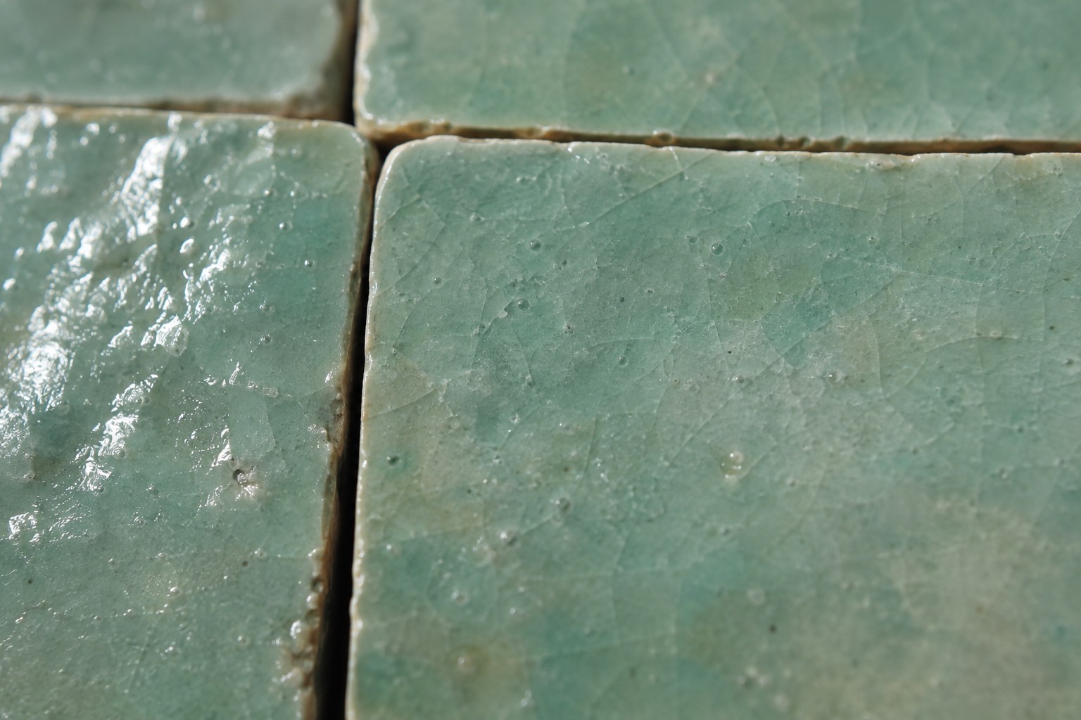 Gros plan sur la texture du zellige émaillé vert d'eau, irrégularités de surface et joints fins